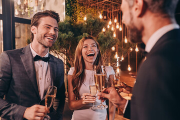 Group of people in formalwear communicating and smiling while spending time on luxury party