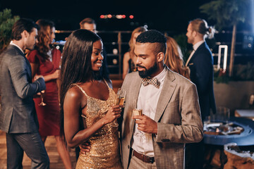 Beautiful young African couple in formalwear holding champagne flutes and smiling