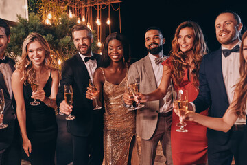 Group of people in formalwear toasting with champagne and smiling while spending time on luxury party
