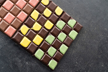 Multicolored fruit chocolate bars on black background. Handmade chocolate with mint, mango, orange, strawberry flavor. Healthy food concept, delicious chocolate sweets for kids, diet, sugar
