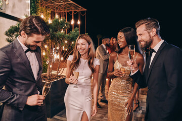 Group of beautiful people in formalwear communicating and smiling while spending time on luxury...