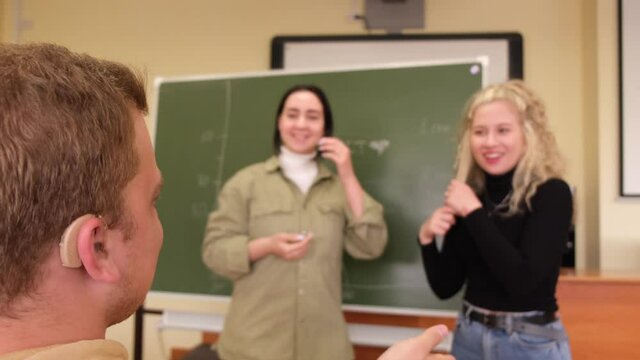 The girls and the guy are talking in Russian sign language. Three deaf students chatting in a university class