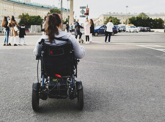 A young disabled woman is sitting in a wheelchair and is preparing to cross the road. Accessibility of public places in everyday life for wheelchair users. 