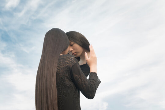 portrait of young woman in black holding large round mirror with her reflection under blue sky