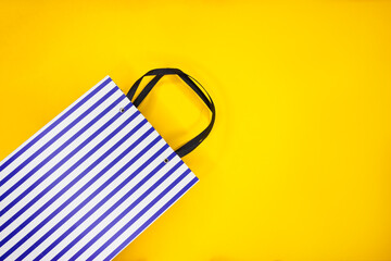 White and blue striped paper shopping bag on yellow background. Black Friday sale shopping.