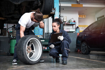 Two mechanic checking wheels at garage, car service technician man and woman checking and repairing the customer car at automobile service center, vehicle repair service shop concept.
