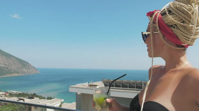 girl drinks a mojito cocktail on the beach, with a view of the sea and mountains