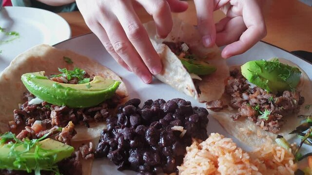 Eating soft shell sirloin beef steak taco with avocado Mexican food full plate