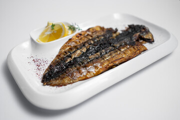 closeup of grilled mackerel fish with lemon on plate on white background