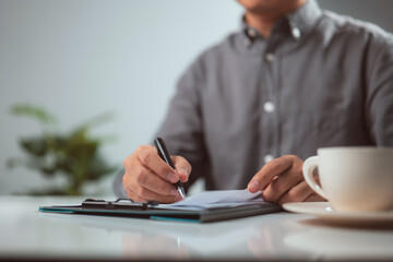 Man hands writing on clipboard with a pen white on desk