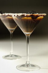 Alcoholic drink based on vodka and coffee liqueur served in a cocktail glass, decorated with chocolate, desiccated coconut and Halloween decoration in the shape of a spider