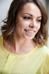 Portrait of cheerful woman with orthodontic brackets. Joyful woman with brown hair showing braces with multicolored rubber bands on her teeth. Concept of stomatology and orthodontic treatment.