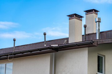 exhaust air pipes and brown rain gutter on private house roof. Metallic Guttering System and...