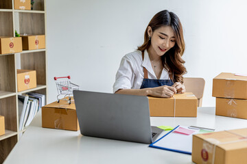 An Asian woman tying a parcel to a customer's box, she owns an online store, she packs and ships through a private transport company. Online selling and online shopping concepts.
