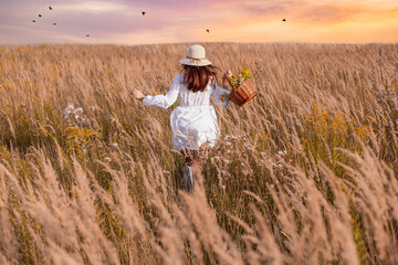 A beautiful woman with a basket of herbs runs in a field of flowers. Herbalist concept, happiness.