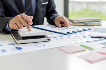 Businessman presses a white calculator, he is the owner of the company, he is checking company financial documents in his office, financial documents show chart format. Concept of financial management