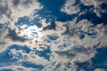 White clouds float in the blue sky. The sun is behind the clouds.