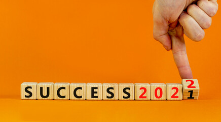 Planning 2022 success new year symbol. Businessman turns a wooden cube and changes words success 2021 to success 2022. Beautiful orange background, copy space. Business, 2022 success new year concept.