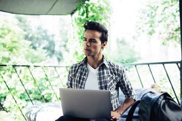 Contemplative Caucasian man with modern laptop technology thinking about program code while working remotely at street terrace, pensive male student with digital netbook e learning in cafe