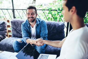 Cheerful Caucaisan colleagues enjoying collaboration for discussing business details during friendly brainstorming meeting in street cafe, successful partners with laptop doing agreement handshake