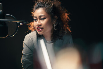 Medium close up candid shot of Asian business woman podcaster broadcasting at in home studio with...