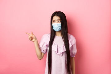 Coronavirus, quarantine and lifestyle concept. Sad and gloomy asian woman in medical mask pointing,...