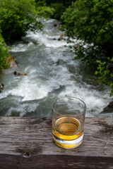 Glass of strong scotch single malt whisky with fast flowing mountain river on background