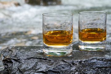 Glass of strong scotch single malt whisky with fast flowing mountain river on background