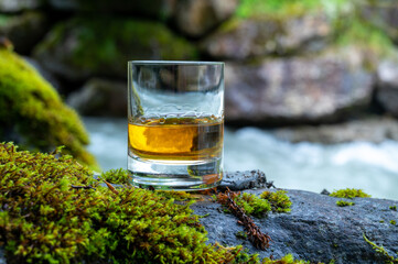 Glass of strong scotch single malt whisky with fast flowing mountain river on background