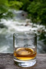 Glass of strong scotch single malt whisky with fast flowing mountain river on background