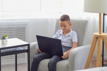 Naklejka premium little schoolboy boy does homework on laptop at home. distance learning concept