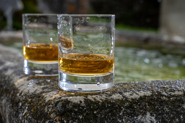 Glasses of strong scotch single malt whisky served on old stone reservoir for water from mountain spring