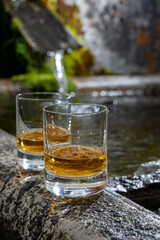 Glasses of strong scotch single malt whisky served on old stone reservoir for water from mountain spring
