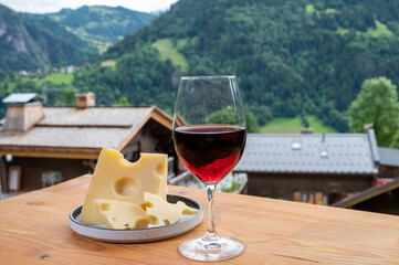 Cheese collection, French cow cheese emmental, glass of red wine from Savoie and french mountains village in Haute-Savoie on background