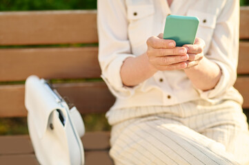 Hands of woman with smartphone sitting on bench