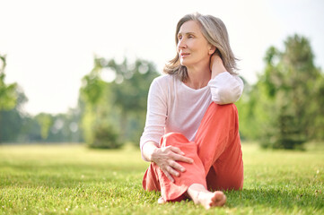Adult pretty woman meditating on lawn in park
