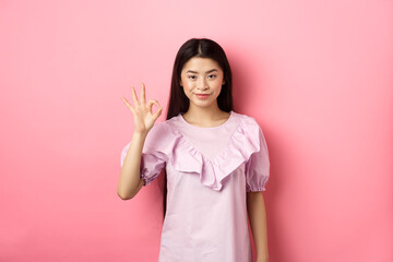 Smiling asian woman in dress showing okay sign, praise and compliment good thing, approve excellent...