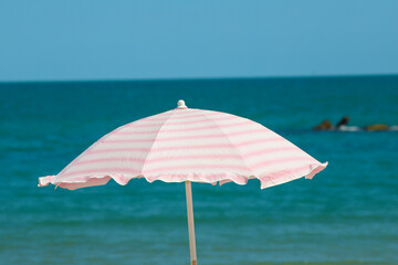 Beach umbrella with pale pink stripes in the foreground, against the blue sea background.