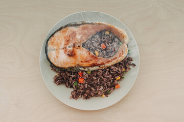 Cooked salmon steak with fried rice on the dish and sealed with plastic.