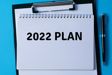 2022 plan written in a notebook on blue background with pen and paper on clipboard.