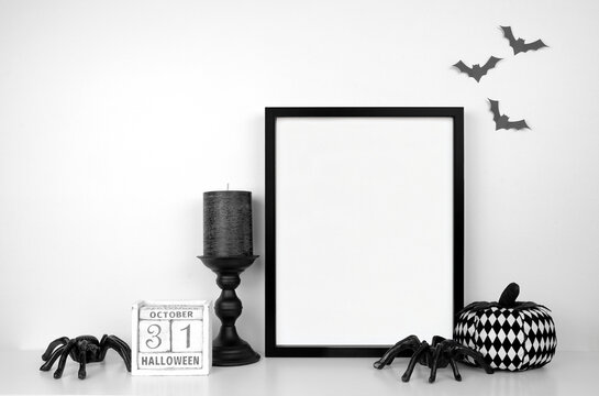 Halloween mock up. Black frame on a white shelf with black and white decor. Portrait frame against a white wall with bats. Copy space.
