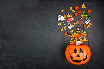 Halloween Jack o Lantern pail with spilling candy, top view on a black background with copy space