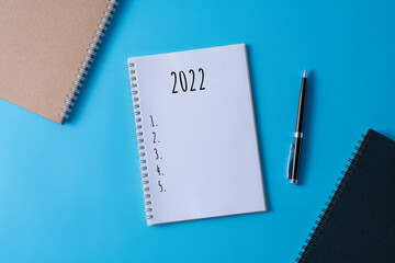 Selective focus of pen and notebook written with 2022 on blue background.