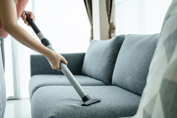 Asian housewife using a wireless vacuum machine to clean a sofa in living room close up. 