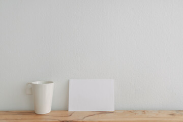 Empty white card mockup lean on a tea cup with white wall background.