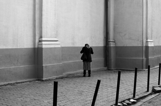 A Poor Woman Standing In Front Of A Wall With Her Head Down, Back View