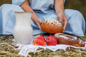 Red apples, fresh homemade bread on a white lace napkin in the hands of a woman in a blue dress. Elements of Russian national cuisine. Photo of food in the autumn.