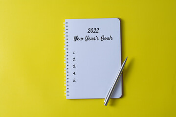 2022 New Year's Goals written in a notebook on yellow background with pen