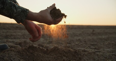Farmer holding ground in hands closeup while sunset. Male hands touching soil on the field during...