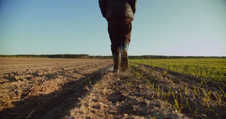 Low angle: man walking in rubber boots in a farmer's field, the blue sky above the horizon. Man...